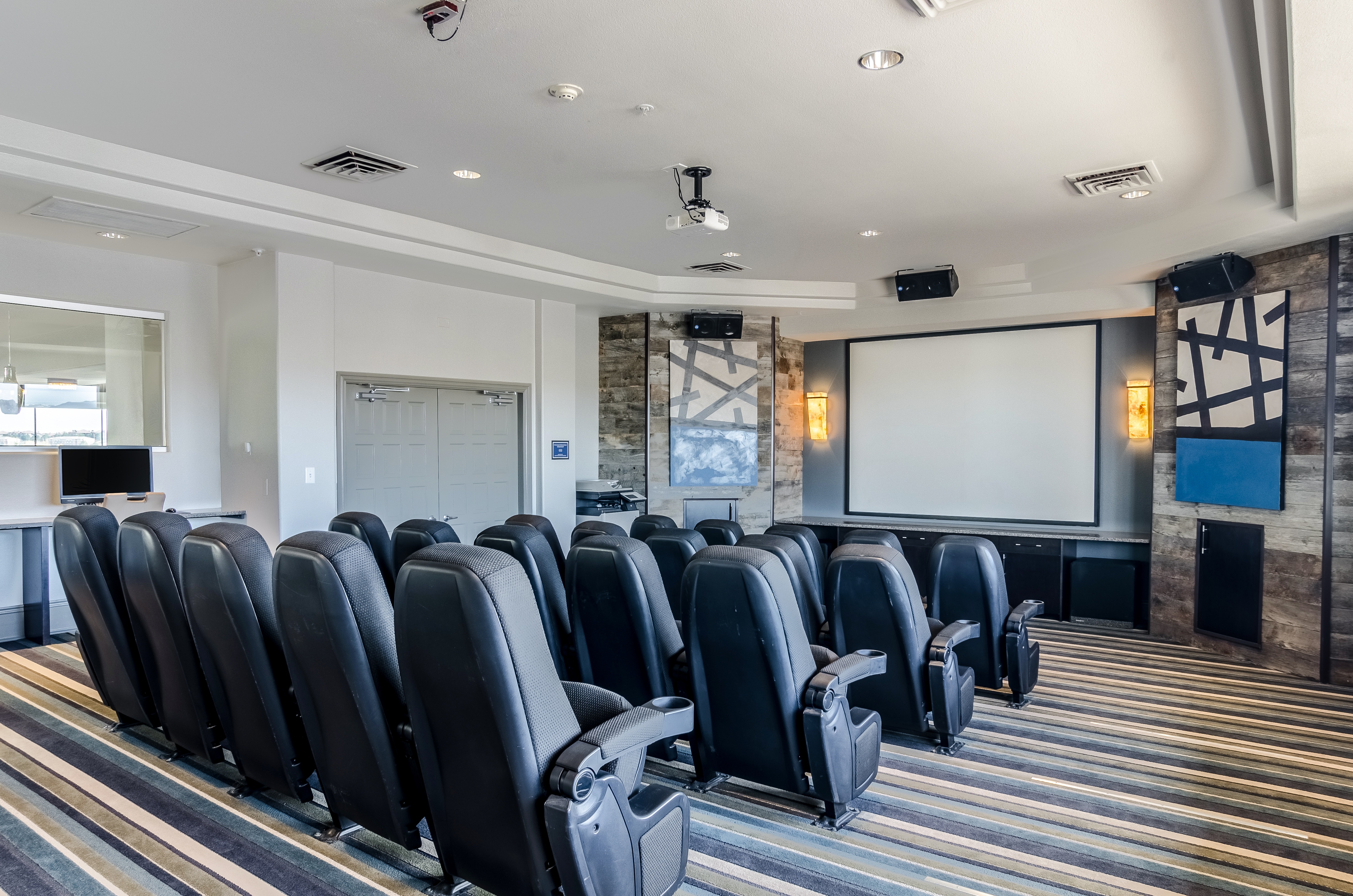 A room with a large movie screen and many black chairs facing the screen.